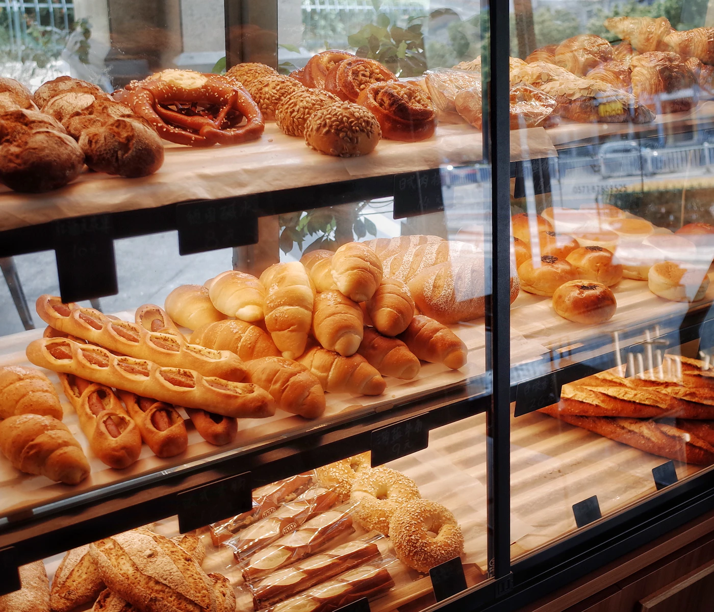 A bakery display case filled with loaves, croissants and buns on wooden shelves