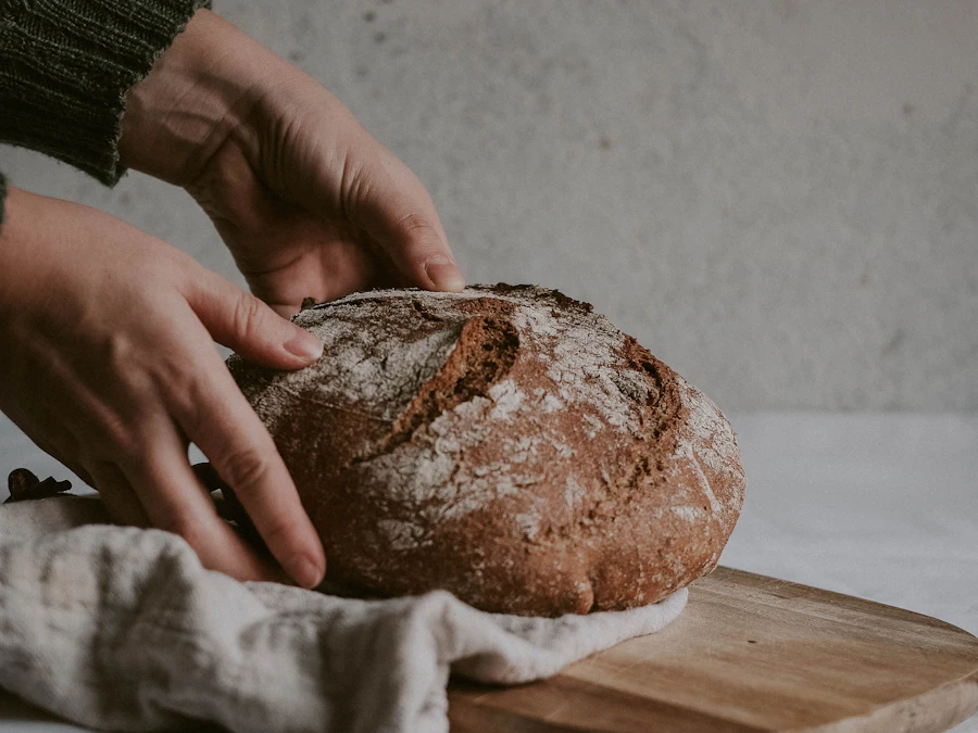 Hands holding a crusty sourdough loaf above a wooden board