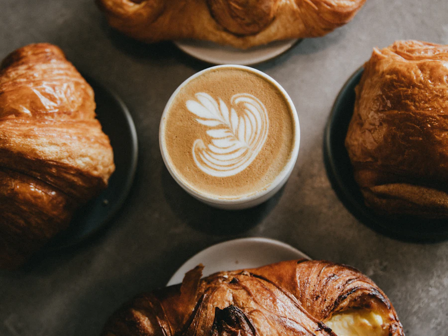 A cup of coffee with latte art surrounded by pastries on a dark table